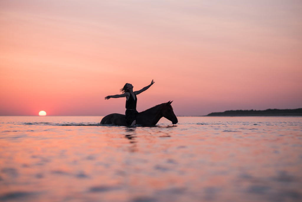 Femme à cheval à l'eau sous un coucher de soleil