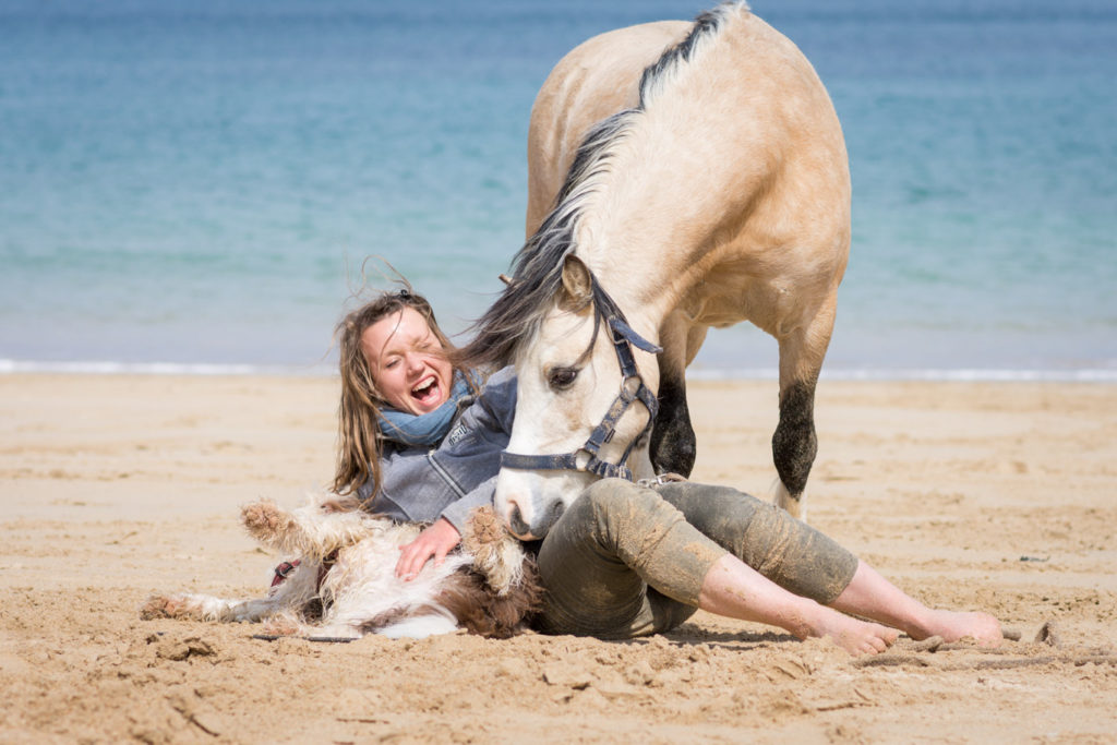 Jeune femme couchée à la plage jouant avec sa chienne et son poney