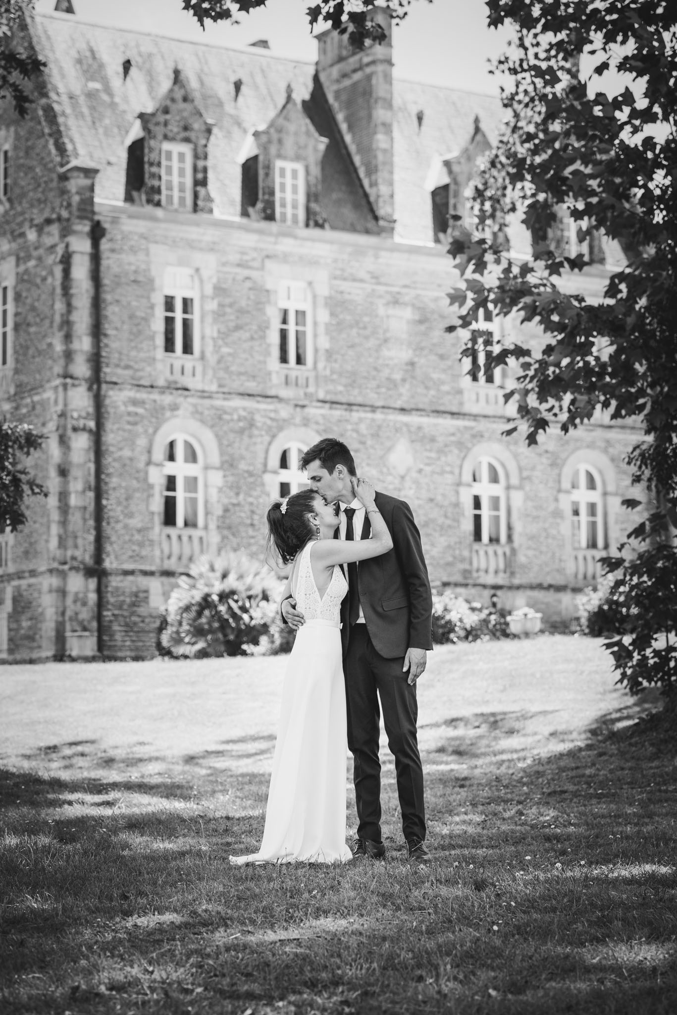Marié faisant un bisou sur le front de la mariée devant un château, photo en noir et blanc