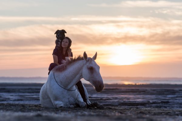 Cavalière sur son cheval gris couché à la plage avec sa chienne sur les épaules