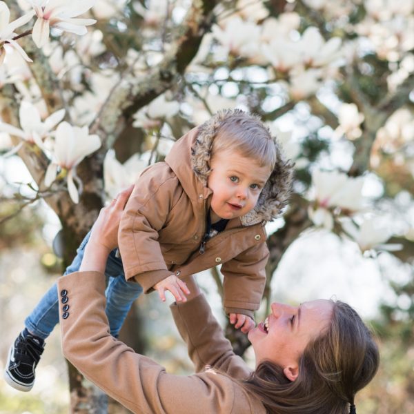 Un maman tenant son fils en l'air sous un magnolia blanc
