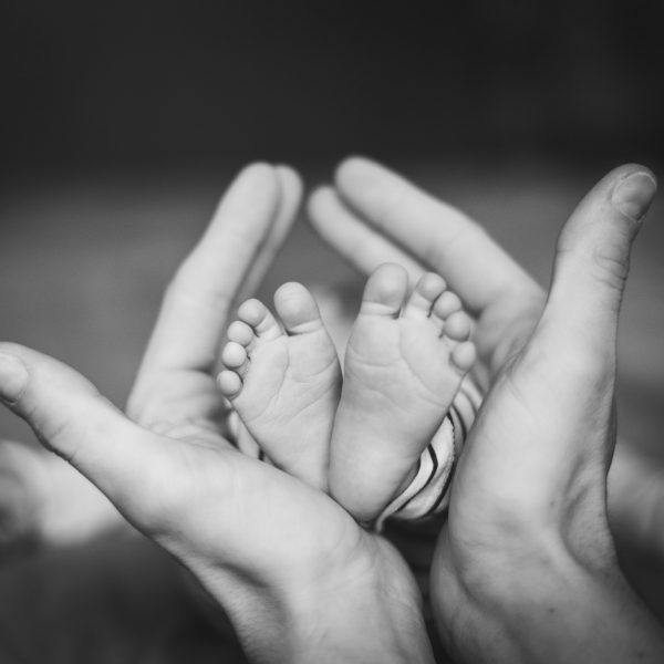 Photo en noir et blanc de pieds de bébé entourés par les mains de ses parents